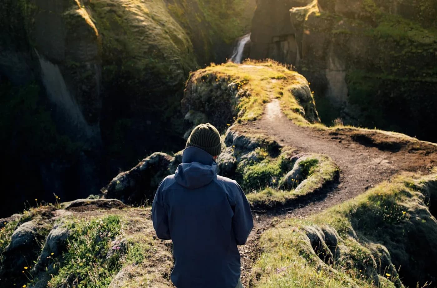 A person walking a narrow path along a green cliff